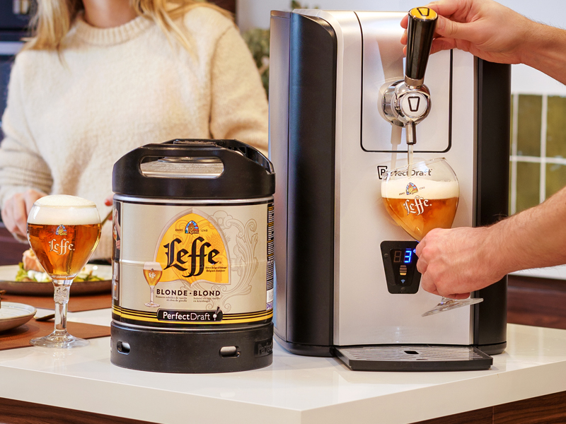 An image of a PerfectDraft home beer machine pouring a Leffe Blonde beer into a Leffe beer glass, with a PerfectDraft keg of Leffe Blonde beside it